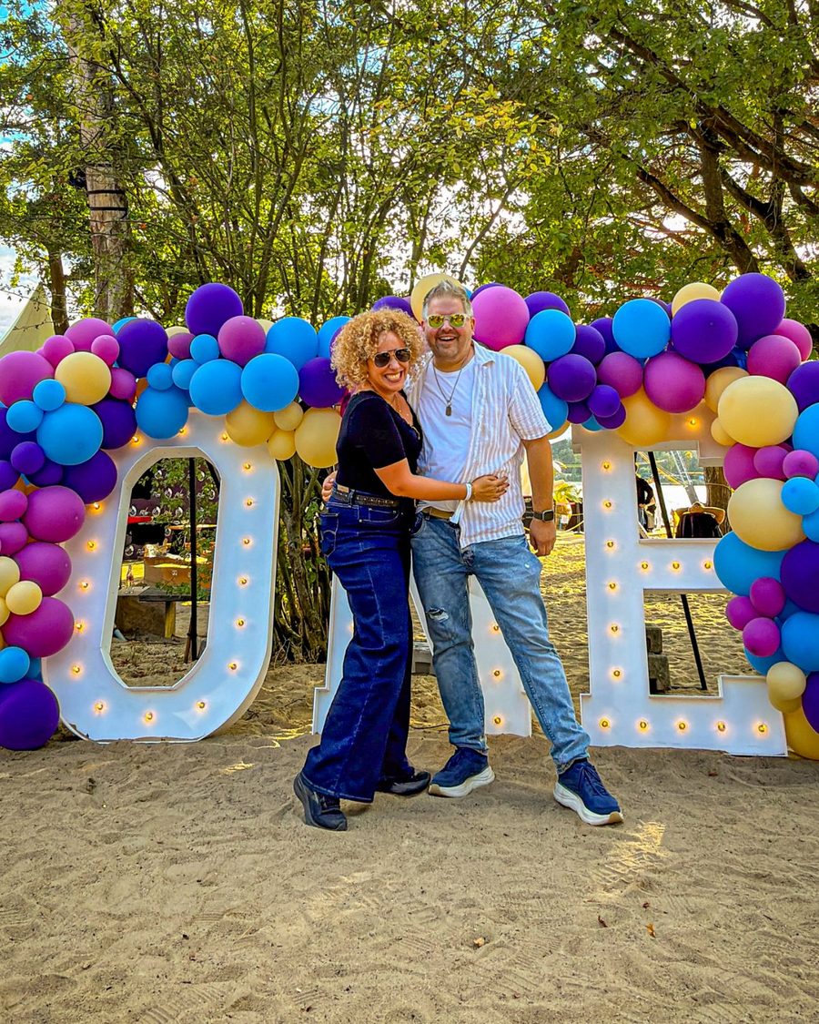 Inga und Björn lachend vor bunten Ballons und Leuchtbuchstaben